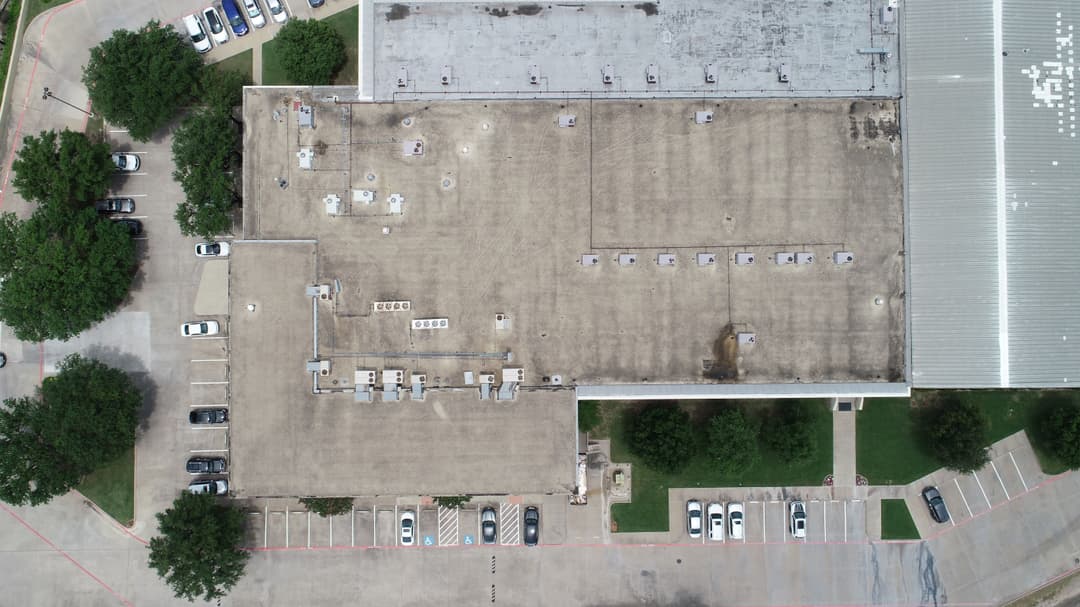 Aerial view of a commercial building rooftop with parking lot and surrounding greenery.