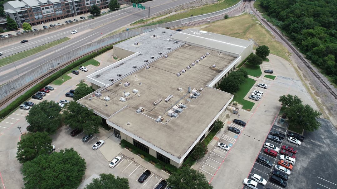 Aerial view of a commercial building with parking lot and surrounding greenery.