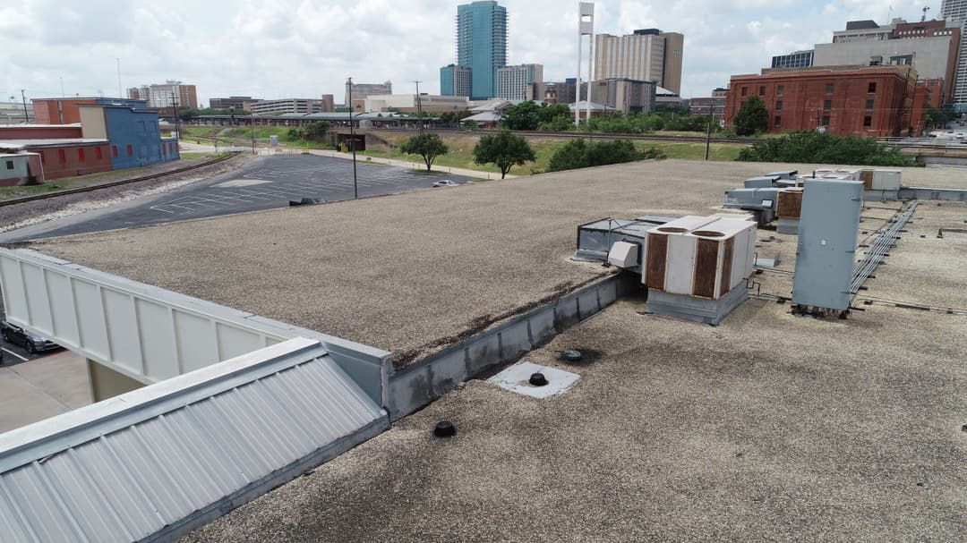 Aerial view of a flat commercial rooftop with HVAC units and city skyline in the background.