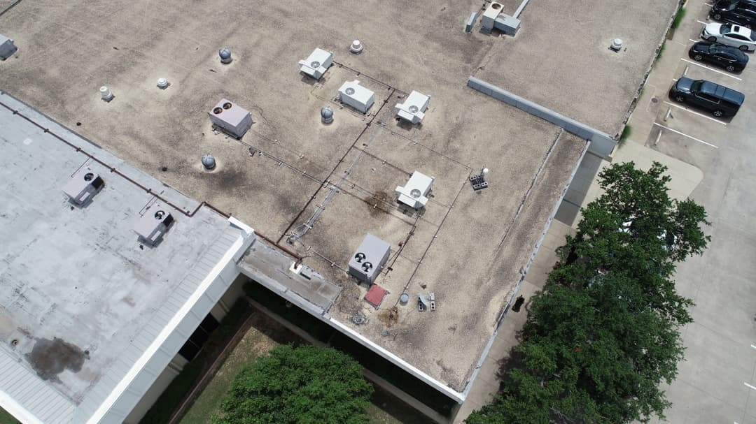 Aerial view of a commercial building rooftop with HVAC units and nearby parking lot.