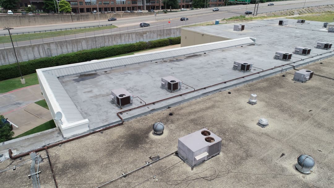 Aerial view of commercial building roof with HVAC units and surrounding landscape.