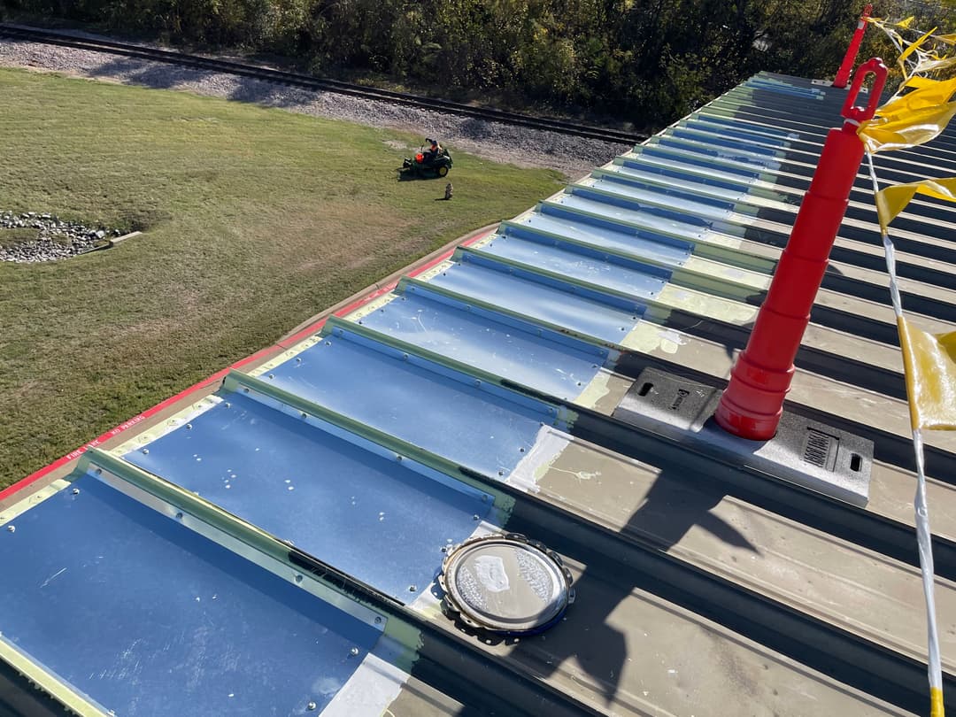 Metal roof installation with flashing on a building, overlooking green lawn and railway tracks.