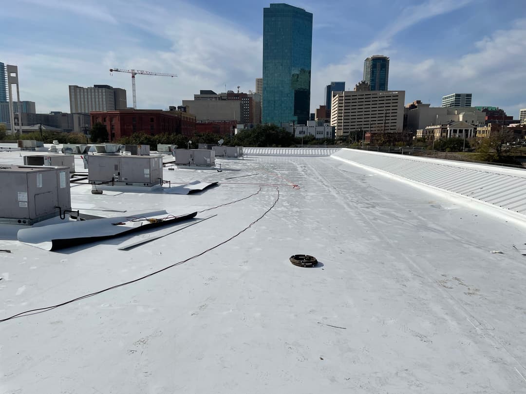 Flat commercial white rooftop with city skyline in the background, featuring HVAC units.