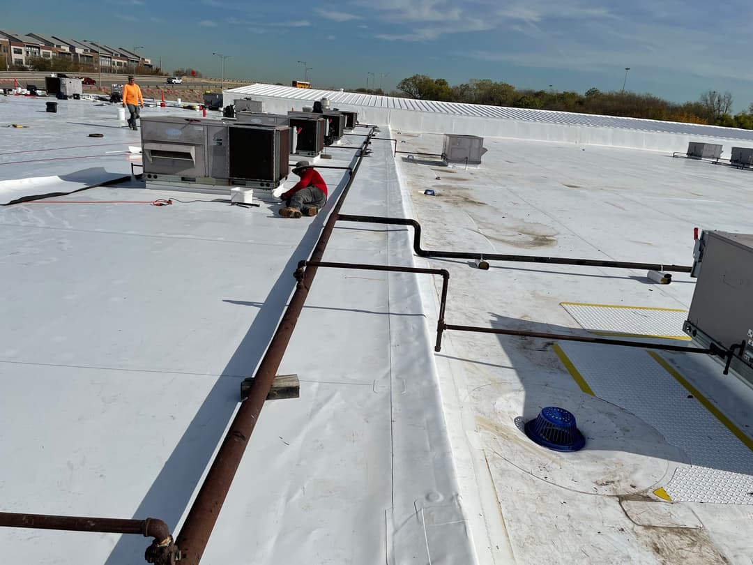 Workers on commercial roof inspecting HVAC units on a clear day with blue sky.