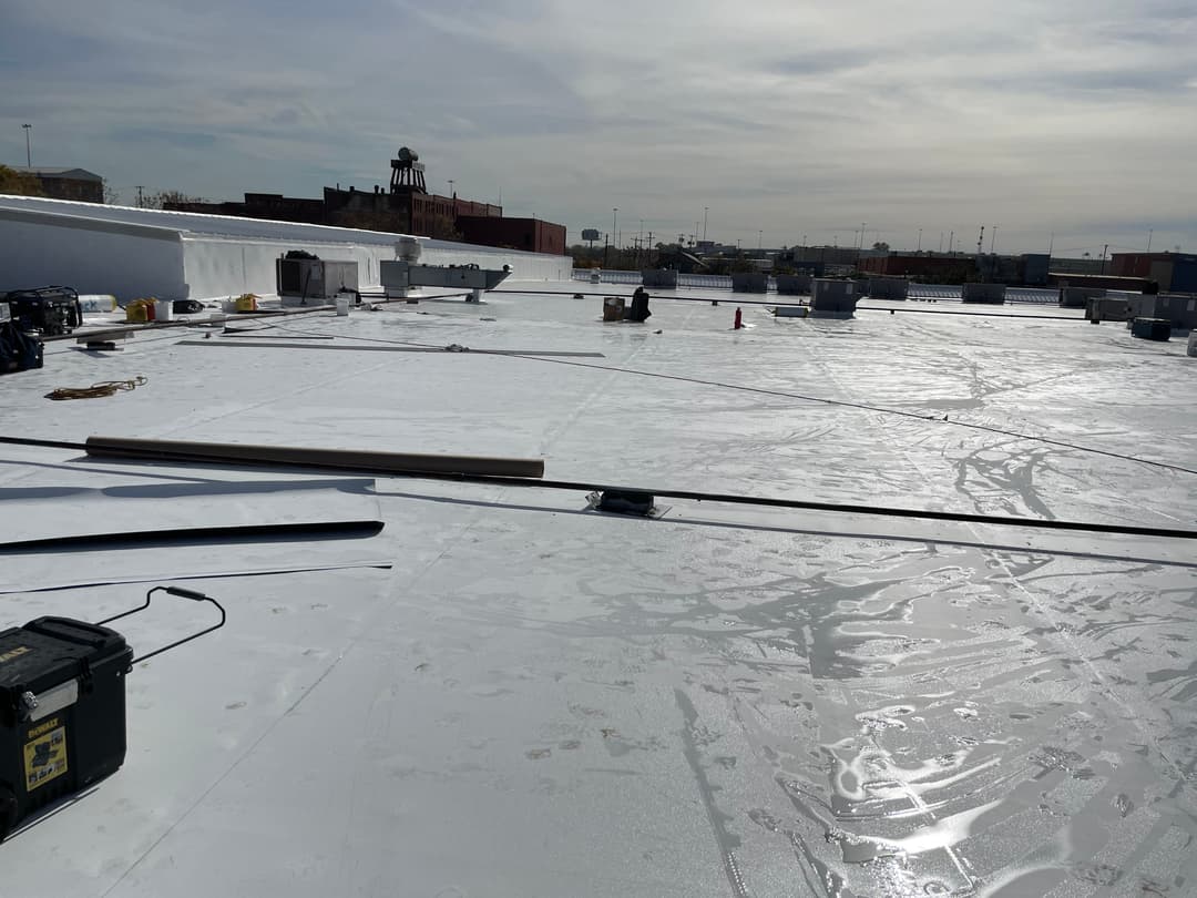 Rooftop with white coating, construction materials, and equipment on a sunny day.
