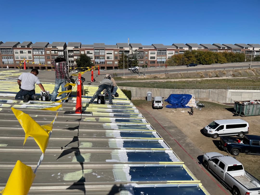 Roofers applying sealant on a commercial building with yellow safety flags in view.