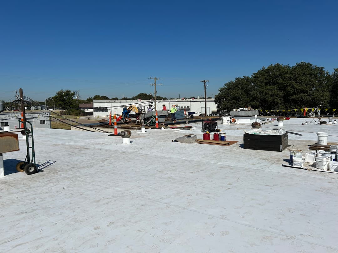 Workers on a commercial roof applying waterproofing materials under clear blue sky.