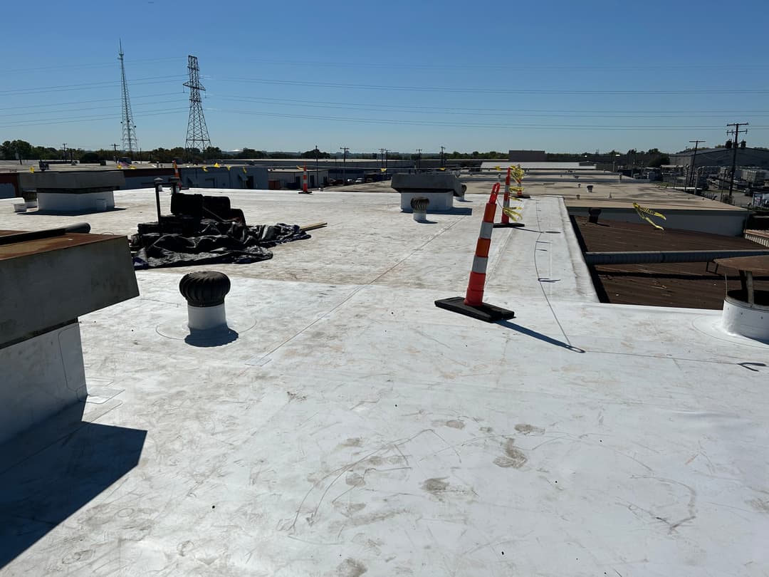 Flat commercial roof with ventilation pipes and safety cones under clear blue sky.