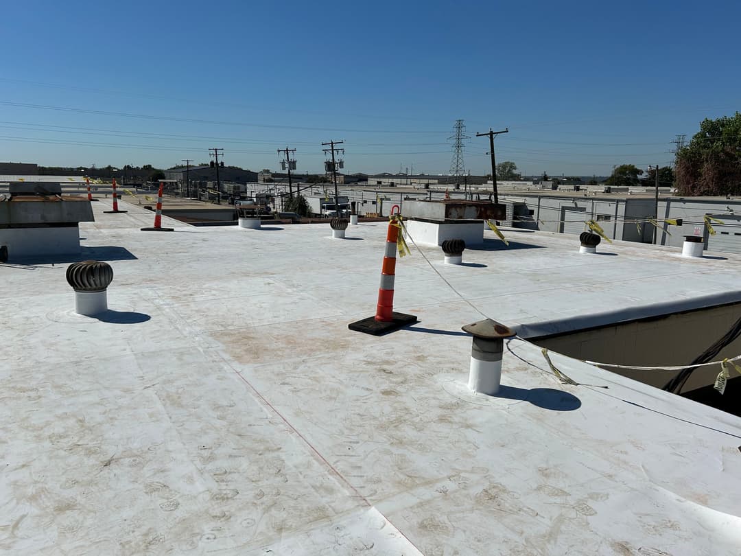 Flat roof with ventilation pipes and safety cones under clear blue sky.