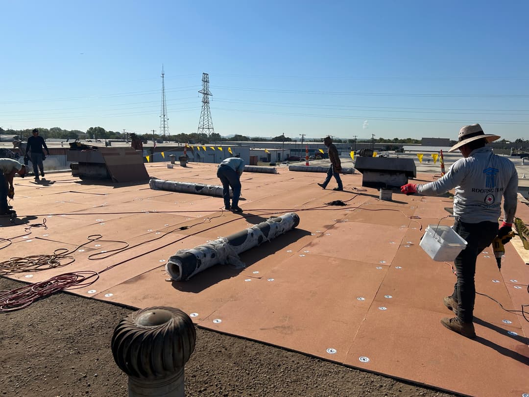 Roofing crew installing new membrane on a commercial building under clear blue skies.