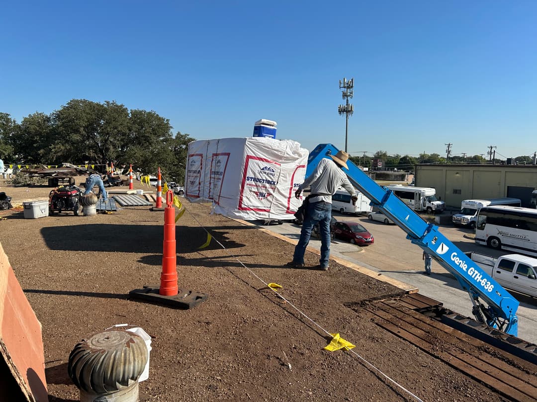 Construction worker using a lift to install materials on a rooftop at a job site.