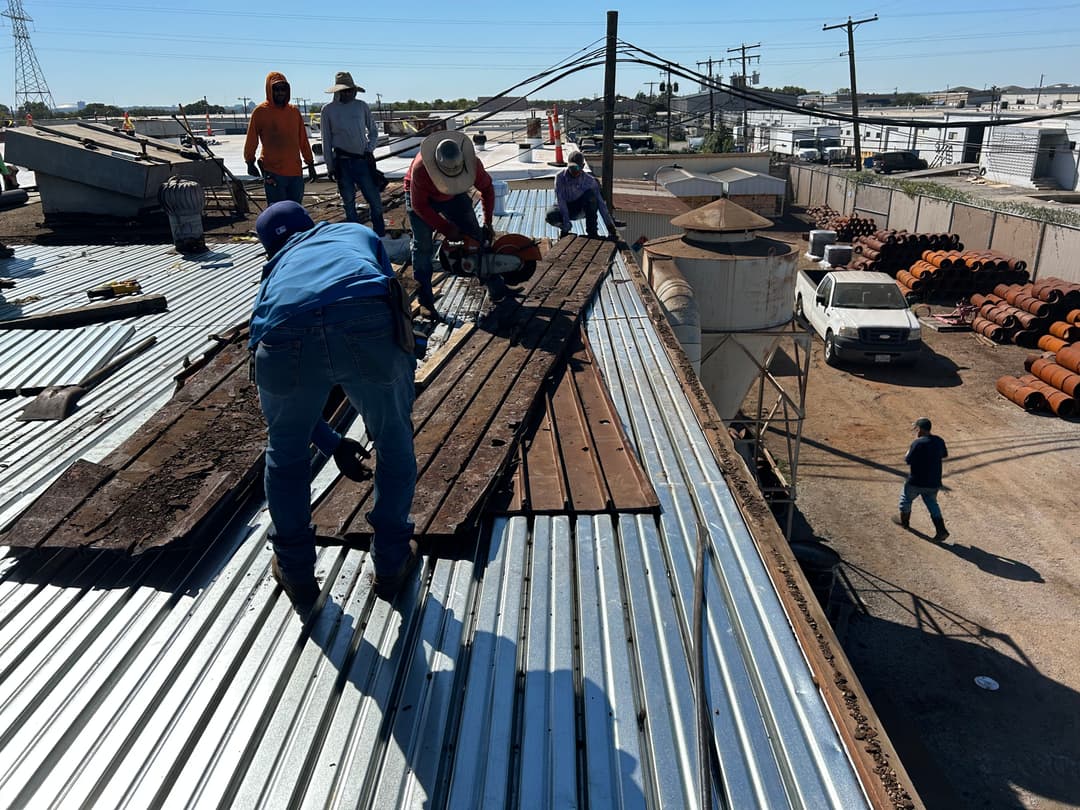 Workers using power tools on a rooftop, assembling materials under clear blue sky.