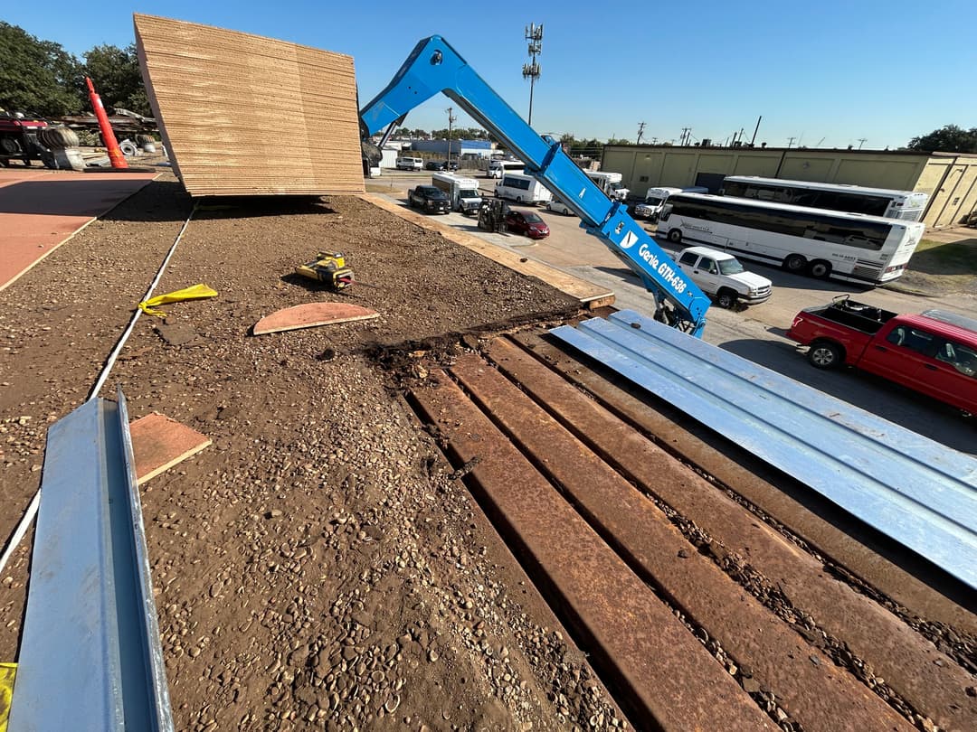 A construction site with machinery lifting plywood sheets onto a building roof.