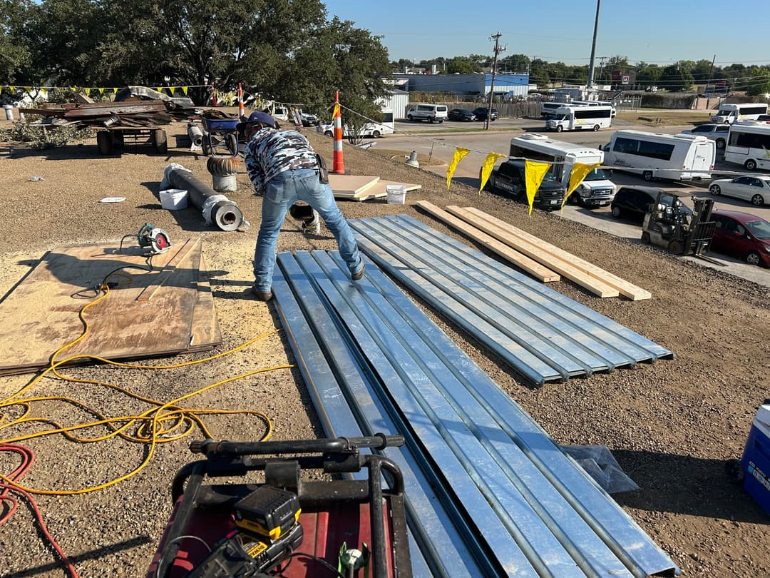 Construction worker organizing metal sheets on a work site with tools and materials visible.