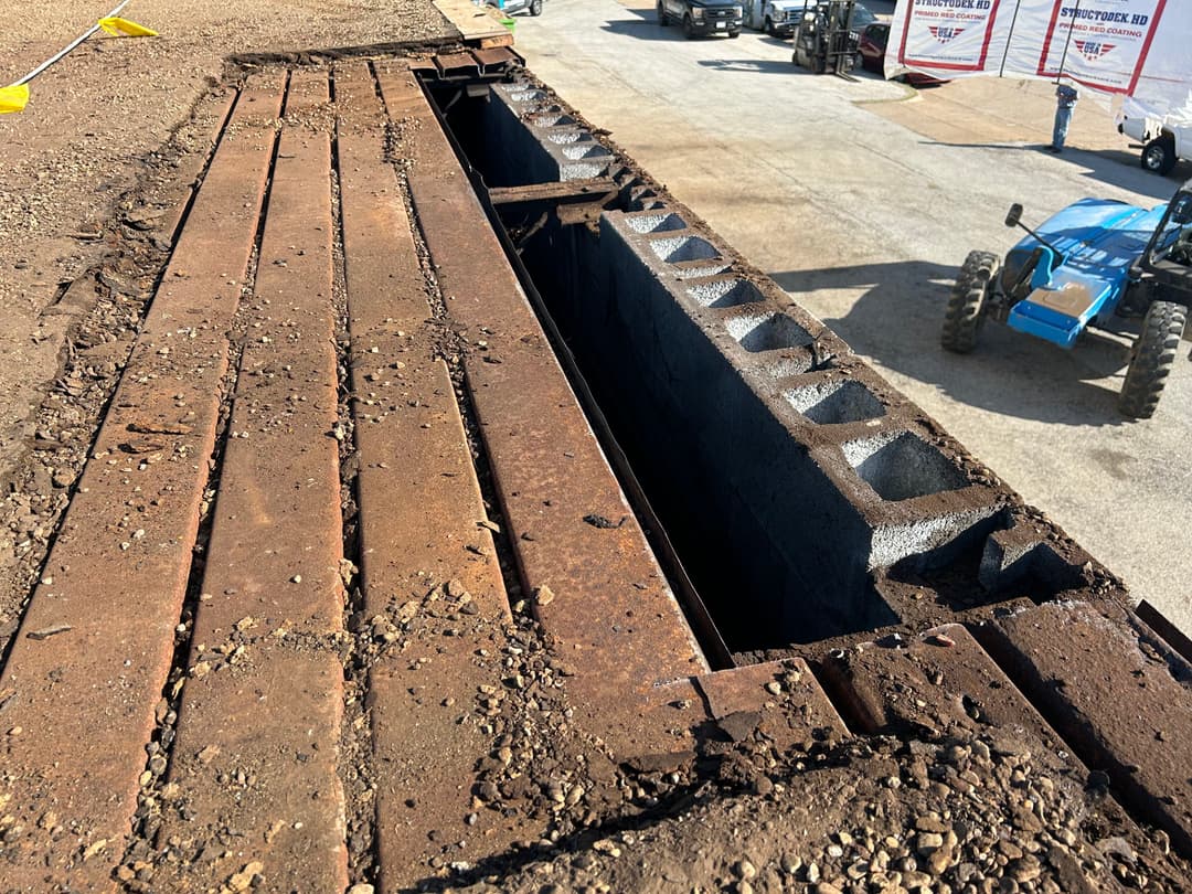 Rusty metal plates covering a deep trench at a construction site with machinery in the background.