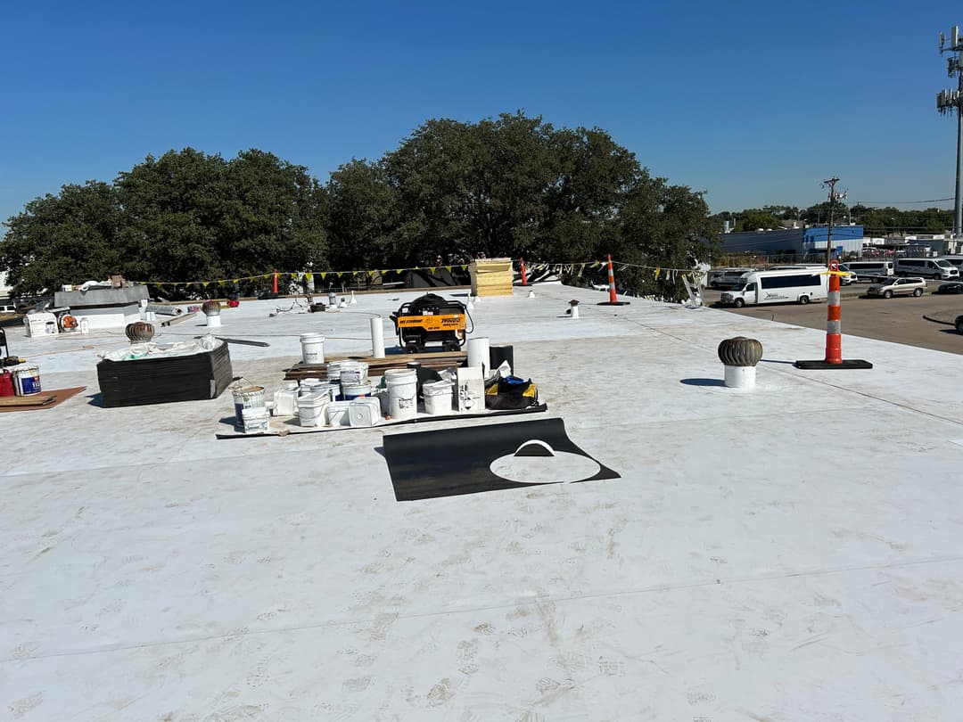 Flat commercial roof with roofing materials and equipment under clear blue sky.