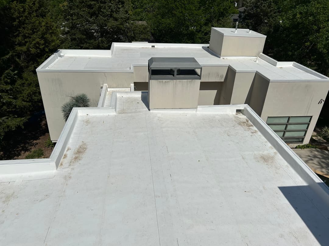 Flat roof of a modern home with a skylight and surrounding trees in view.