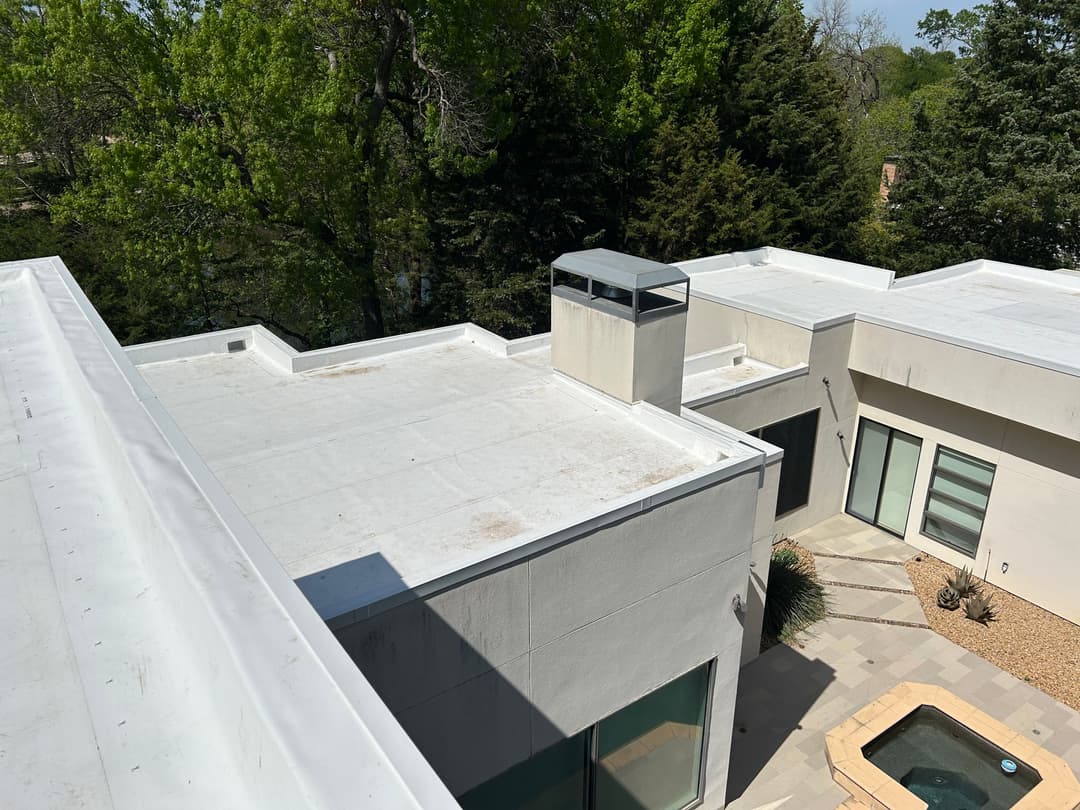 Modern flat roof design with white coating, overlooking trees and a small patio area.