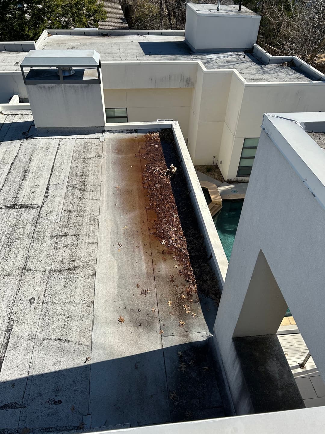 Overhead view of a flat roof showing dirt, leaves, and rust stains near a pool.