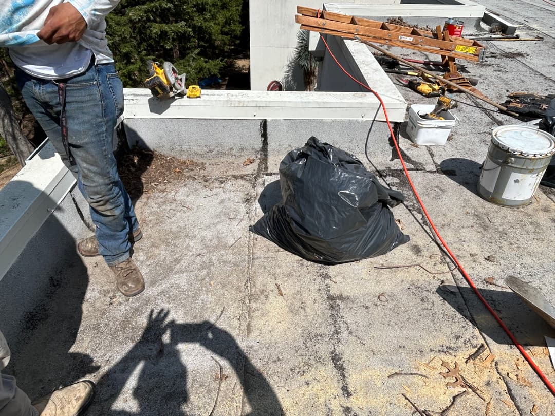 Construction workers on a roof, with tools and a black trash bag on a flat surface.
