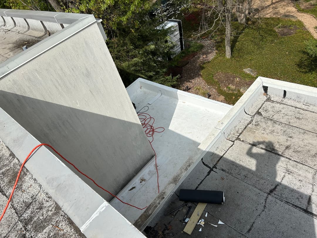 Aerial view of flat roof with drainage, tools, and extension cord on a residential building.