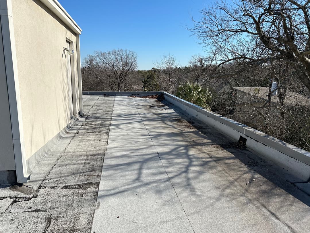 Flat rooftop view with clear sky, trees, and shadow patterns creating a serene atmosphere.