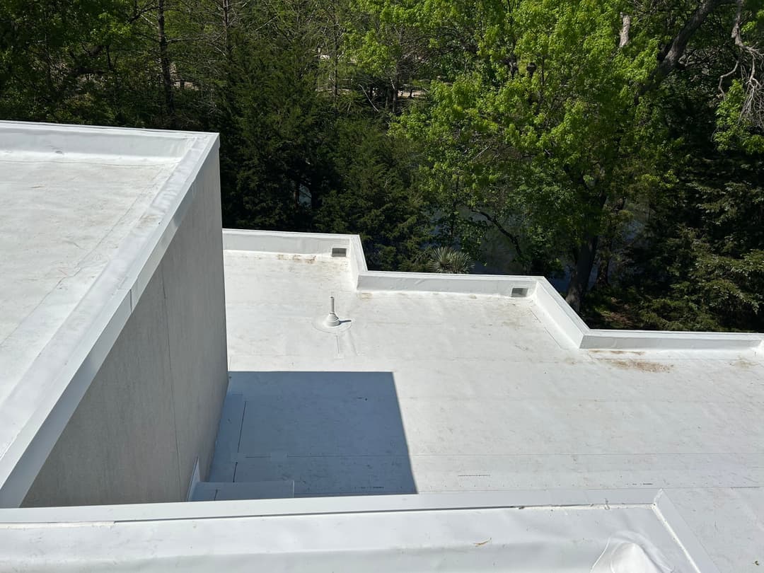 Flat white rooftop with drainage details, surrounded by green trees and a serene landscape.