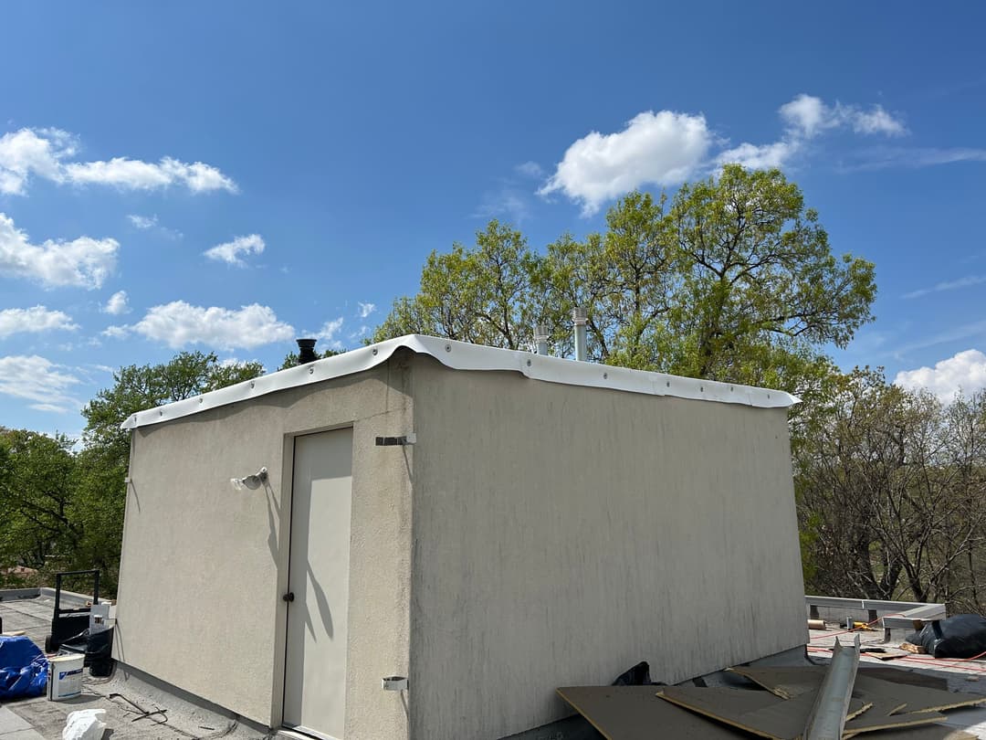 Rooftop view of a white building with a flat roof and trees under a clear blue sky.