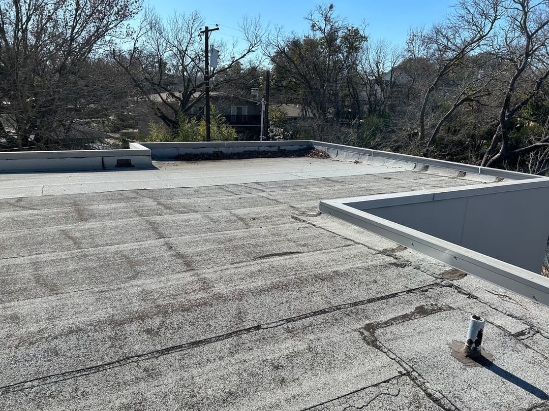 Flat commercial roof with visible wear, surrounded by trees and utility poles.