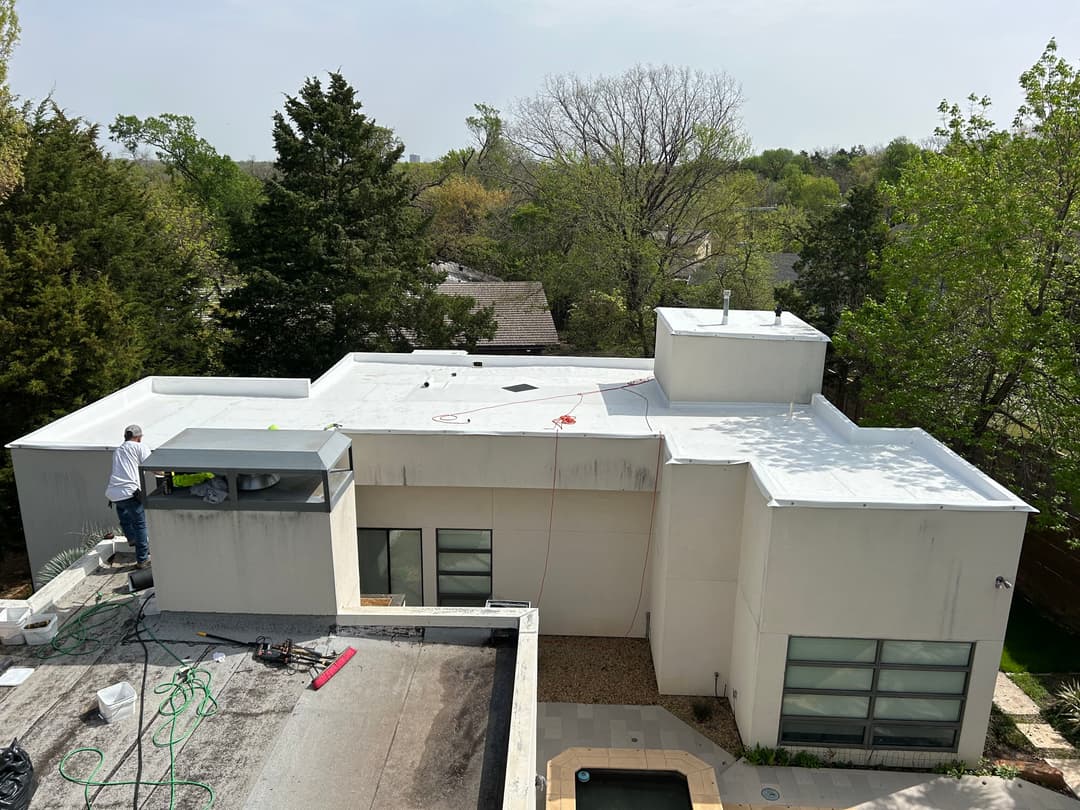 Aerial view of a flat roof being maintained, surrounded by greenery and modern architecture.