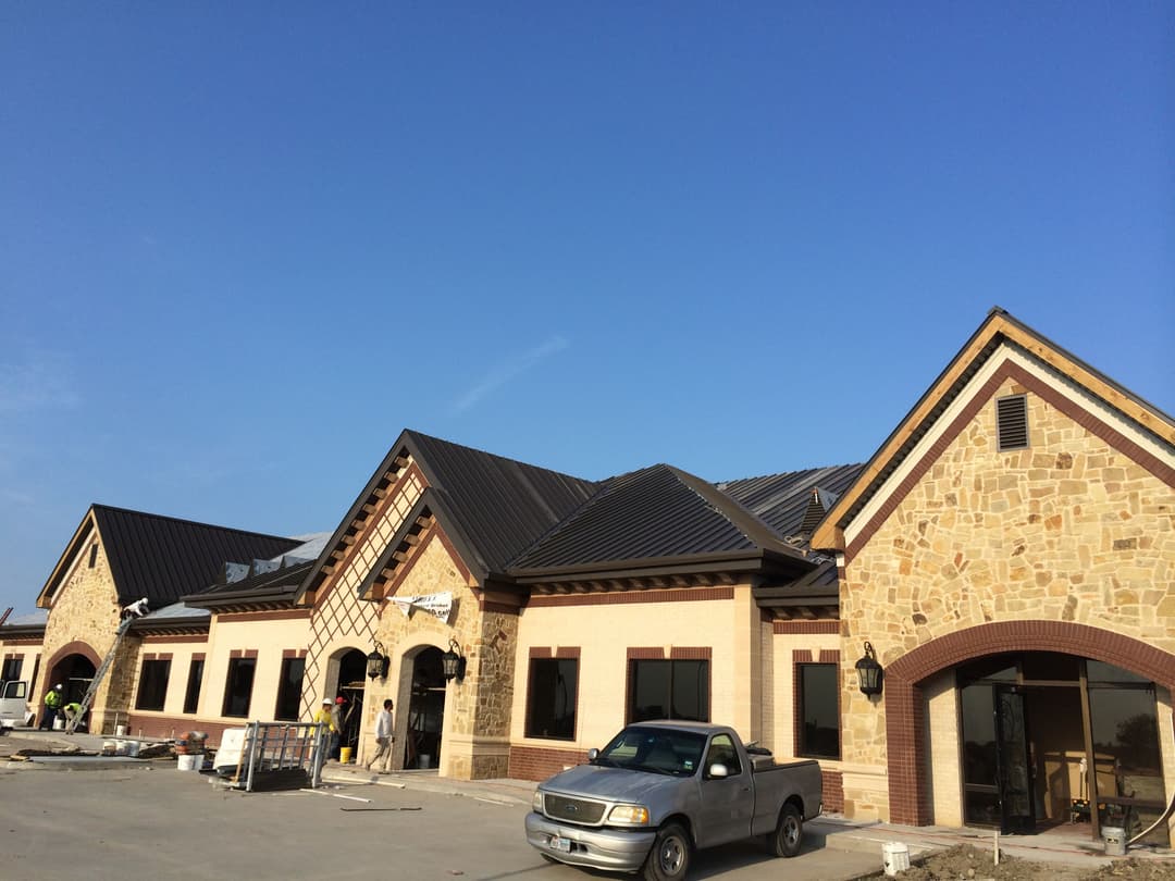 New commercial building under construction with stone accents and metal roof against blue sky.