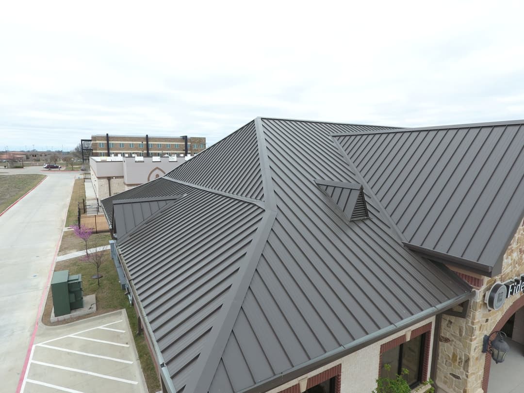 Aerial view of a modern building with a metal roof and surrounding landscape.