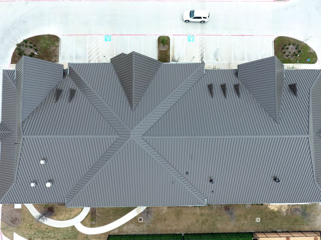 Aerial view of a modern building with a dark metal roof and landscaped surroundings.