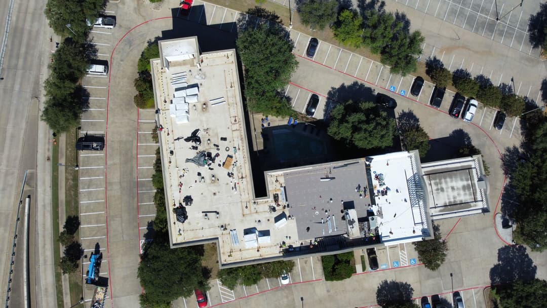 Aerial view of a commercial building with rooftop work and surrounding parking lot.