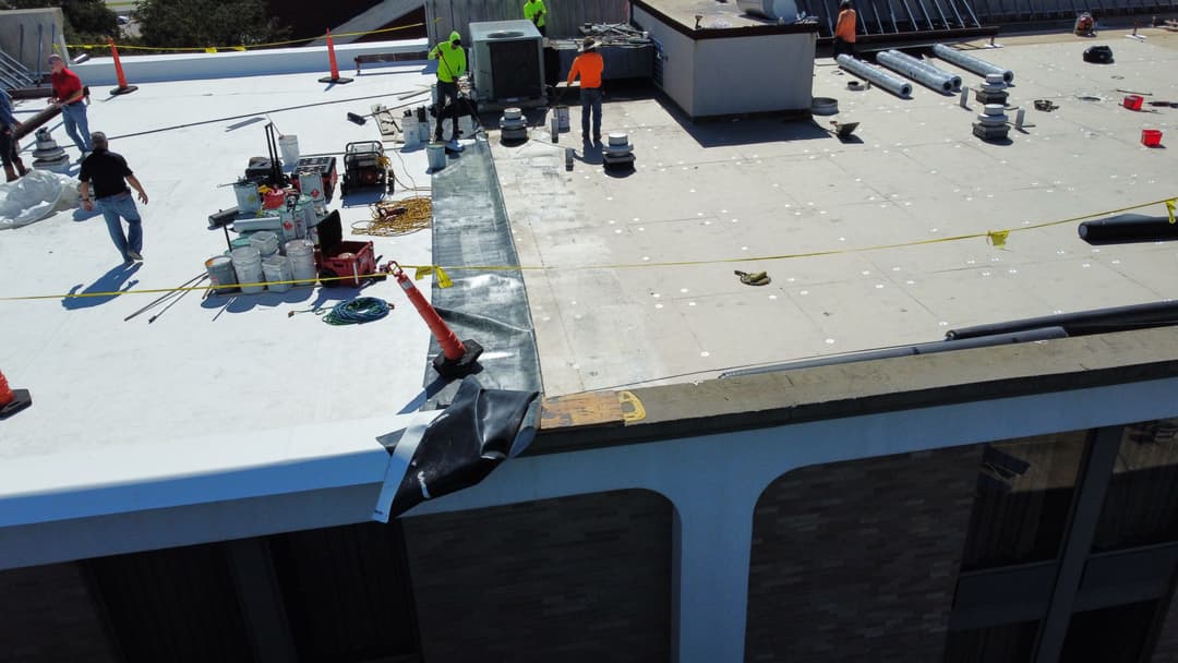Workers performing roofing maintenance on a commercial building rooftop, tools and materials visible.