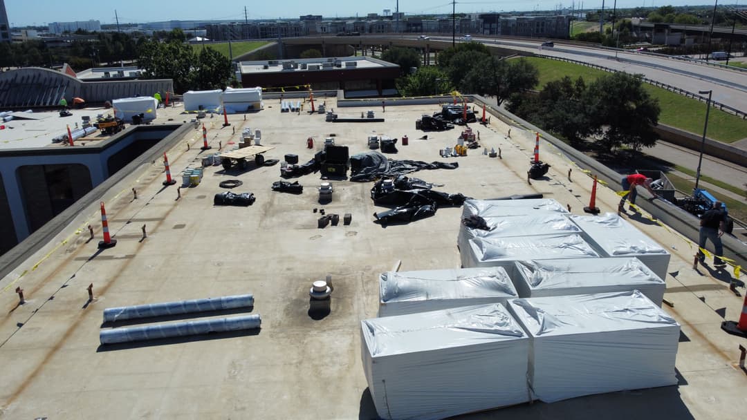 Construction site with wrapped materials and equipment on a rooftop, surrounded by safety barriers.