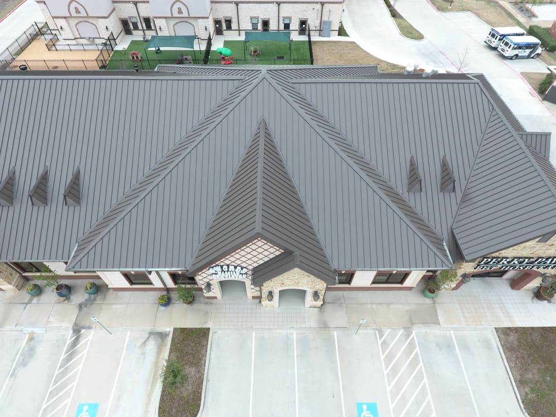 Aerial view of a modern building with a distinctive metal roof and parking lot.