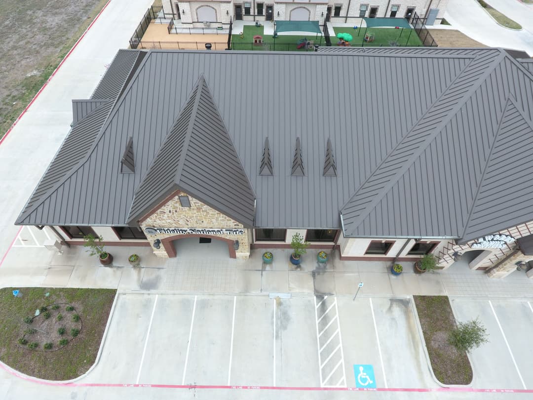 Aerial view of a modern building with a metal roof and landscaped parking area.