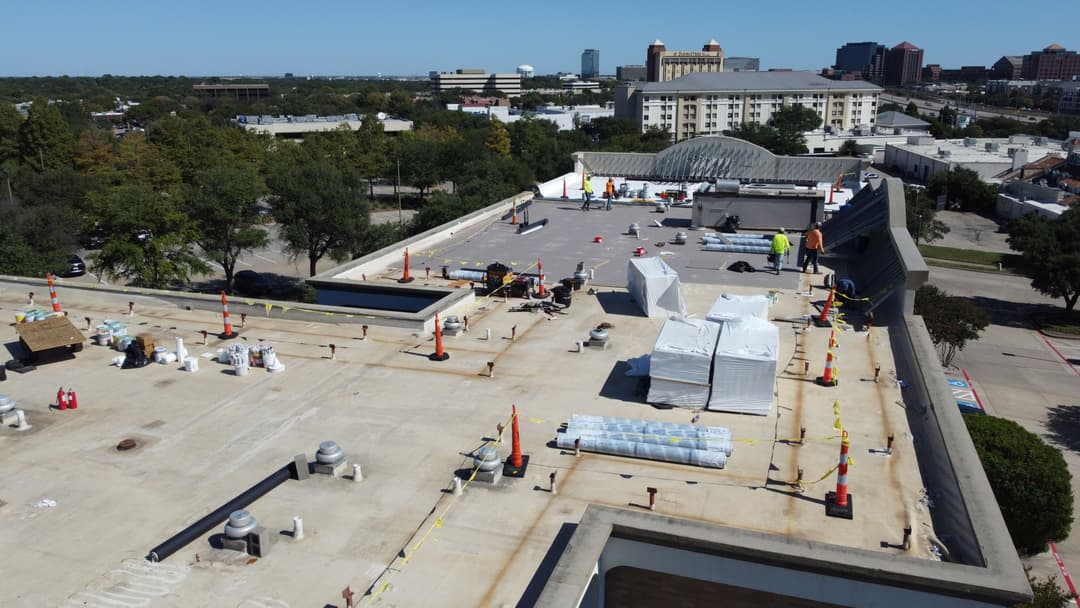 Aerial view of a commercial roof under construction with workers and materials visible.