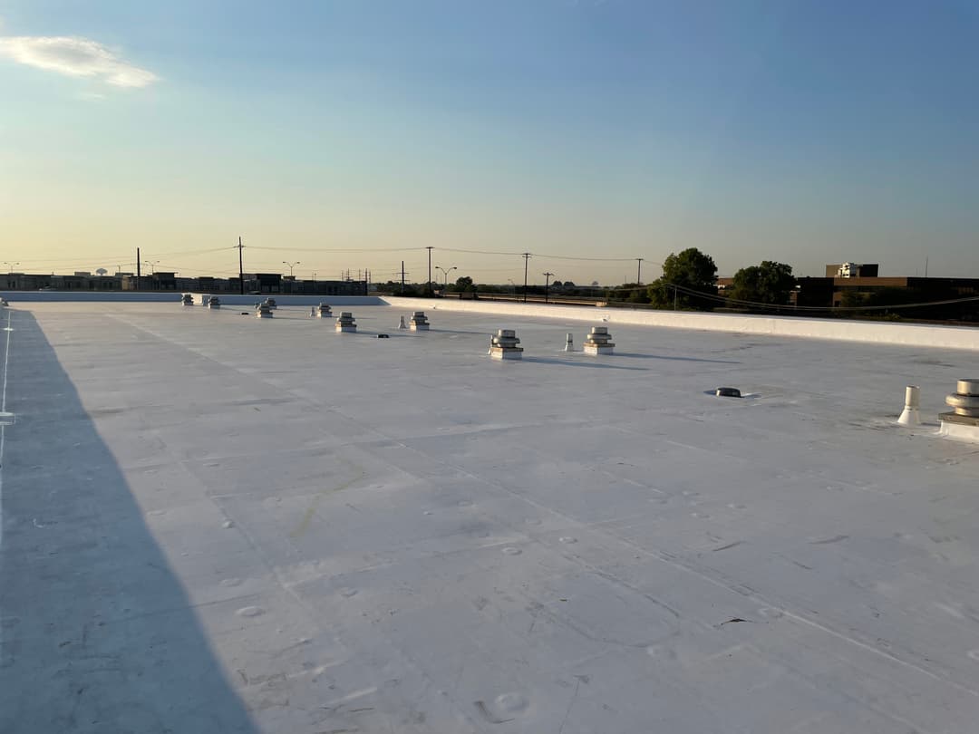 Flat commercial roof with ventilation pipes, bathed in sunset light.