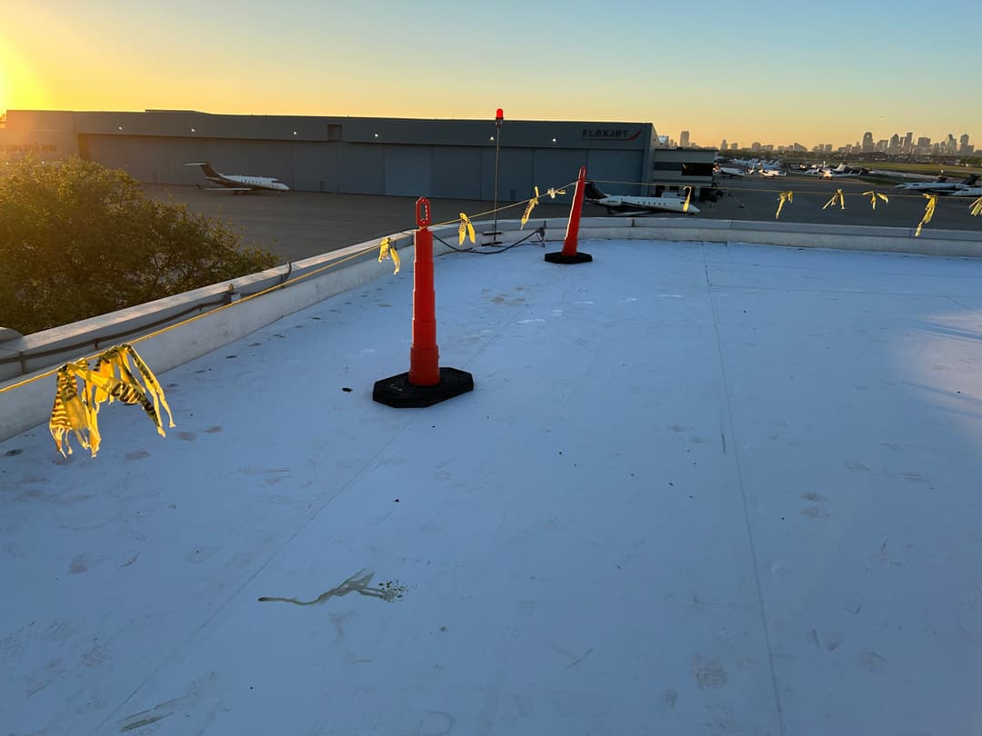Sunset view from a rooftop with safety cones and caution tape; planes in the background.