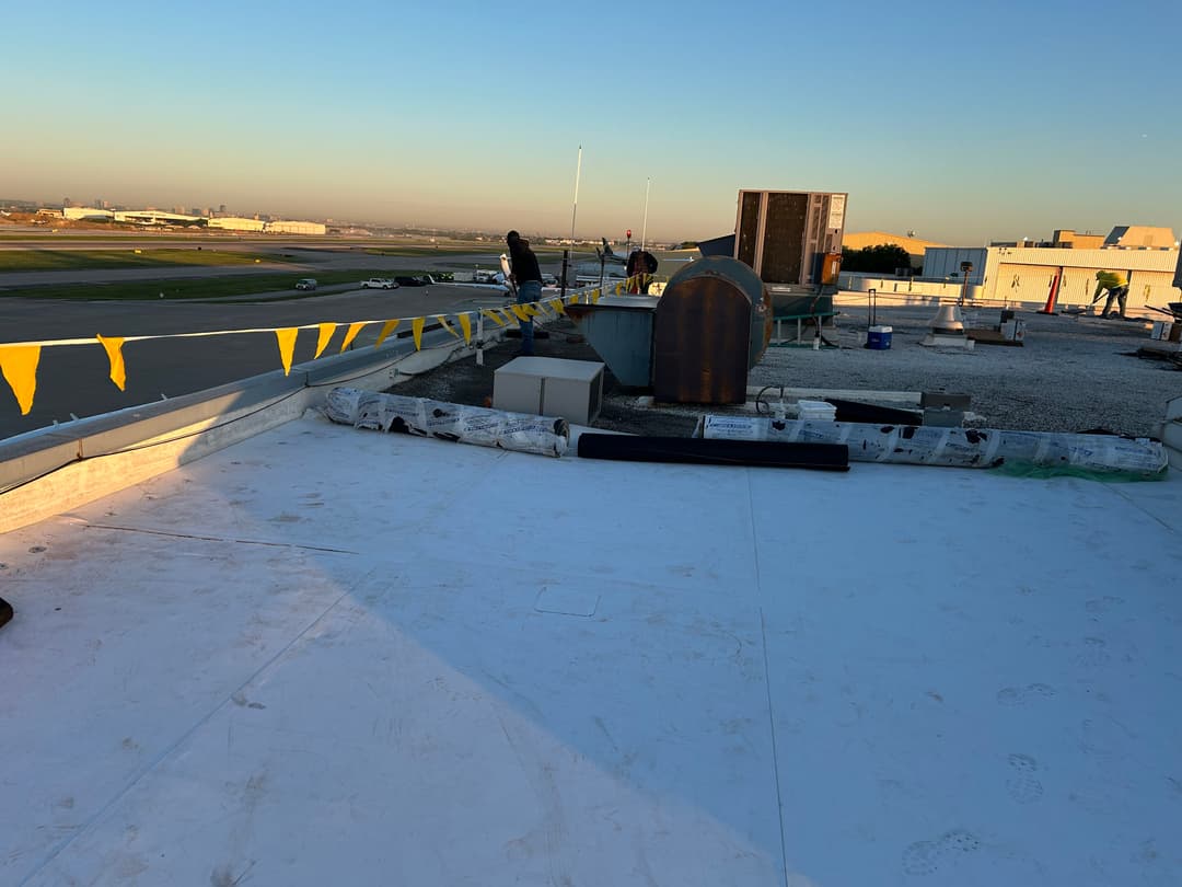 Workers on a rooftop with construction materials and an airport view during sunset.