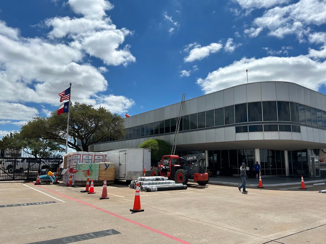 Construction equipment and supplies at a modern building under a blue sky with clouds.