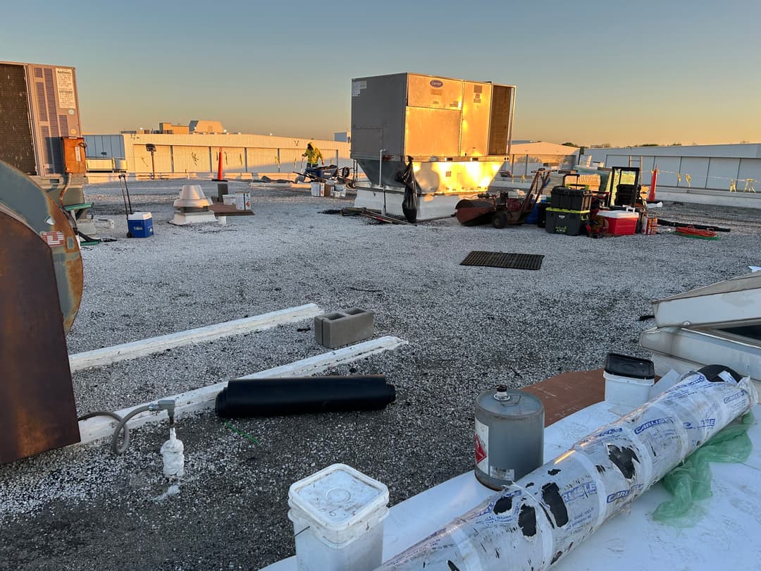 Roofing work site with HVAC units, tools, and materials under a clear sky.