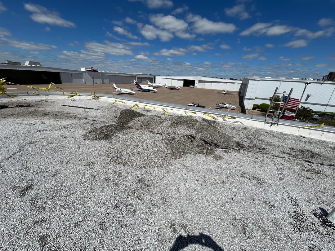 Gravel roof on a building with small airplanes parked in the background under a blue sky.