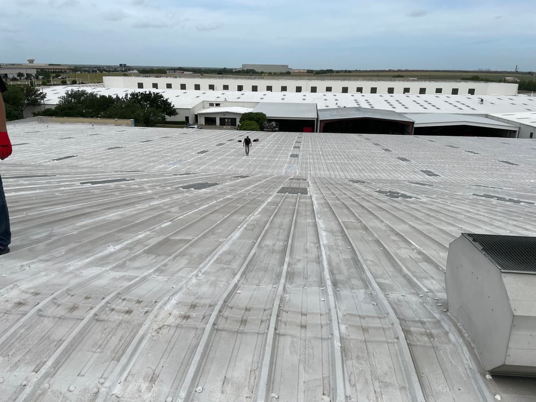 Person walking on a wide industrial metal rooftop with cloudy sky above.