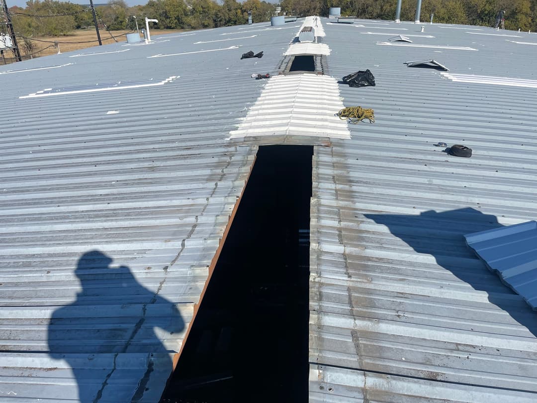 View of a roof with a large opening, debris scattered, and a person's shadow present.