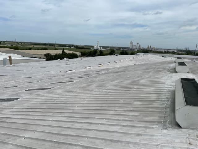 Aerial view of a white roof with skylights against a cloudy sky and industrial background.
