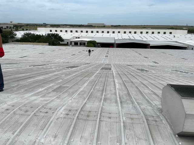 Person walking on a commercial roof with white surface and industrial building in background.