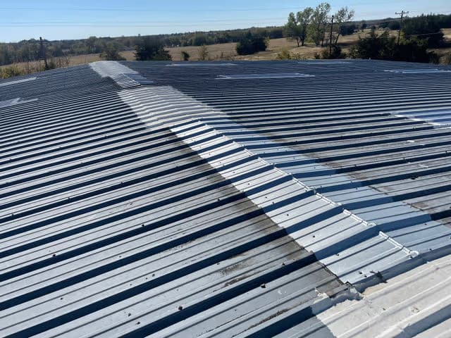 Metal roof with visible seams and sunlight over a rural landscape.
